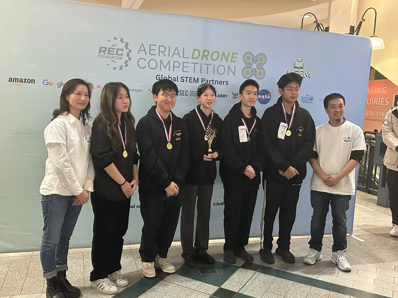 Squad 1368B in front of the Aerial Drone Competition backdrop at the Vancouver qualifier, wearing medals and holding a trophy, two of them wearing 1368B badges.