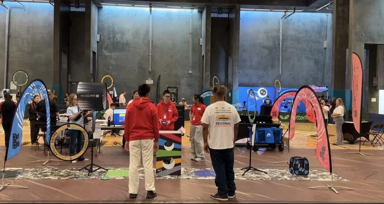 The championship floor in San Diego: hoop gates on stands, team tables and banners across an indoor hall.